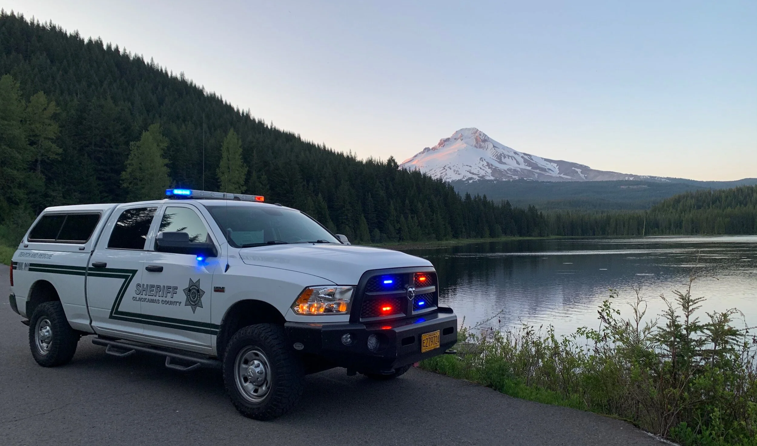 Clackamas County Sheriff search-and-rescue truck beside a lake, forest and snow-covered mountain.