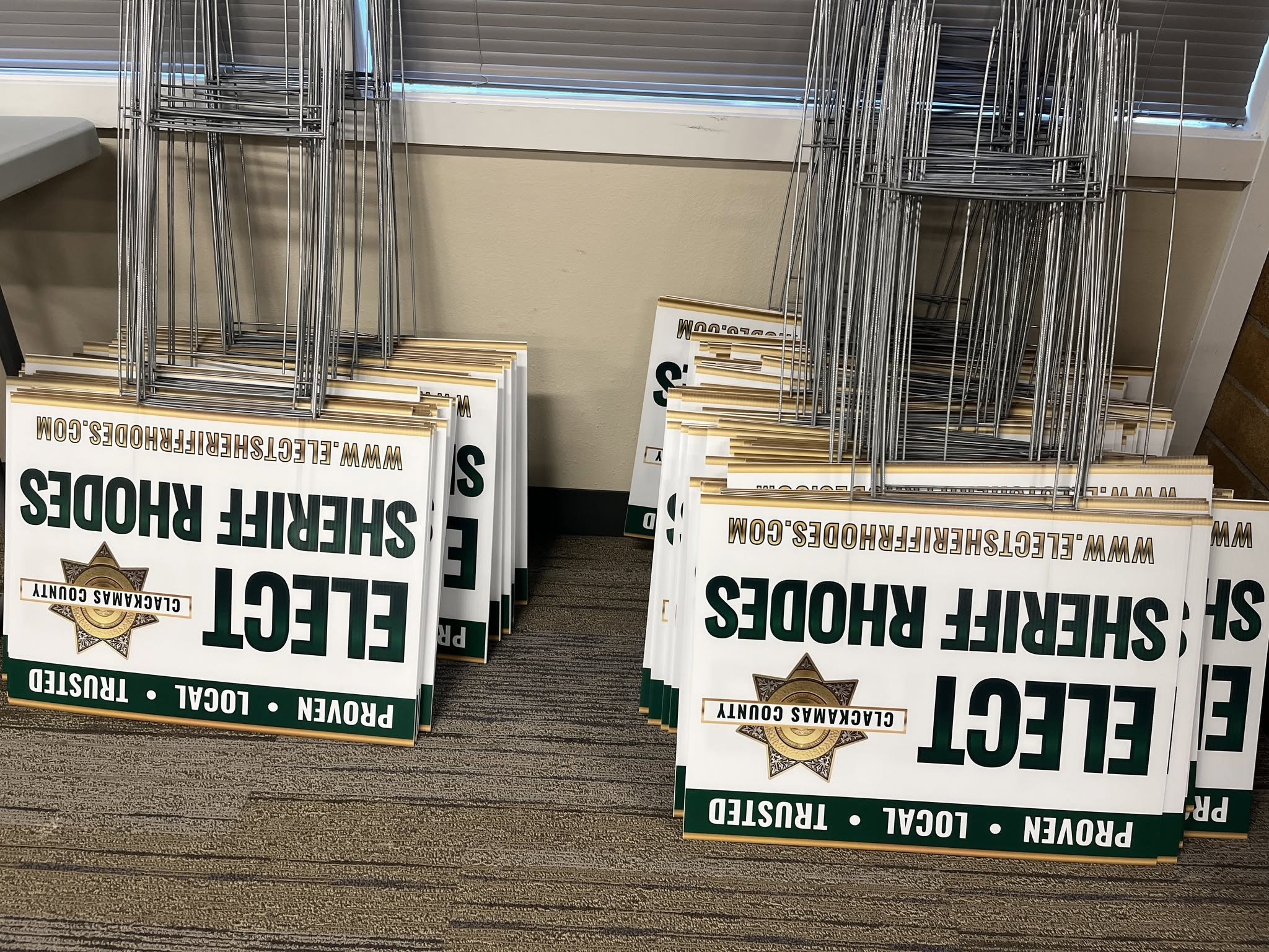 Stacks of Elect Sheriff James Rhodes campaign signs and metal wire frames beside windows.